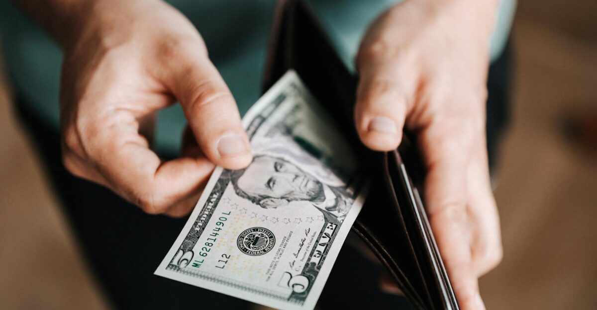 A person taking a five dollar bill from a wallet symbolizing personal finance and budget management