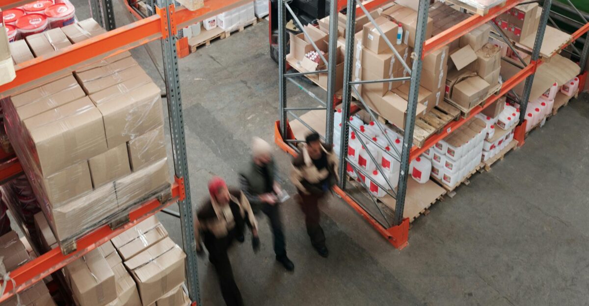 A high angle view of workers in motion in a busy warehouse with shelves full of boxes and packages