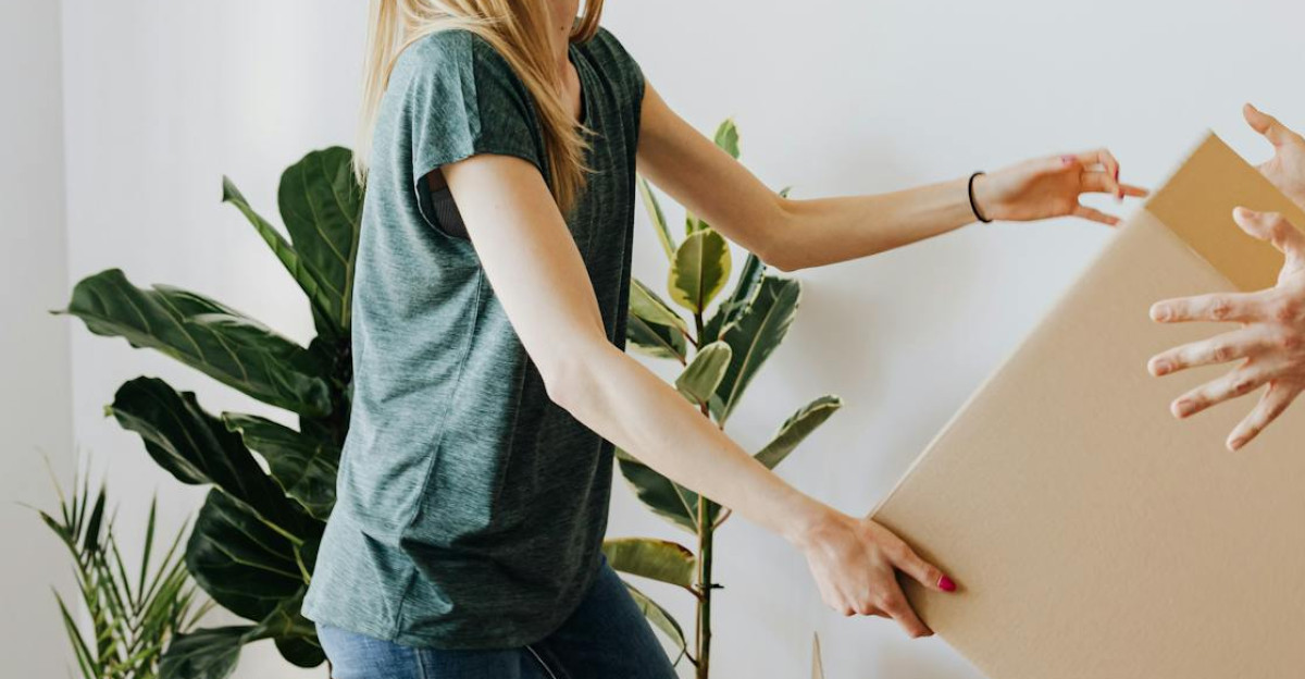Side view serious couple wearing jeans and shirts carrying cardboard boxes with belongings while moving into new apartment together
