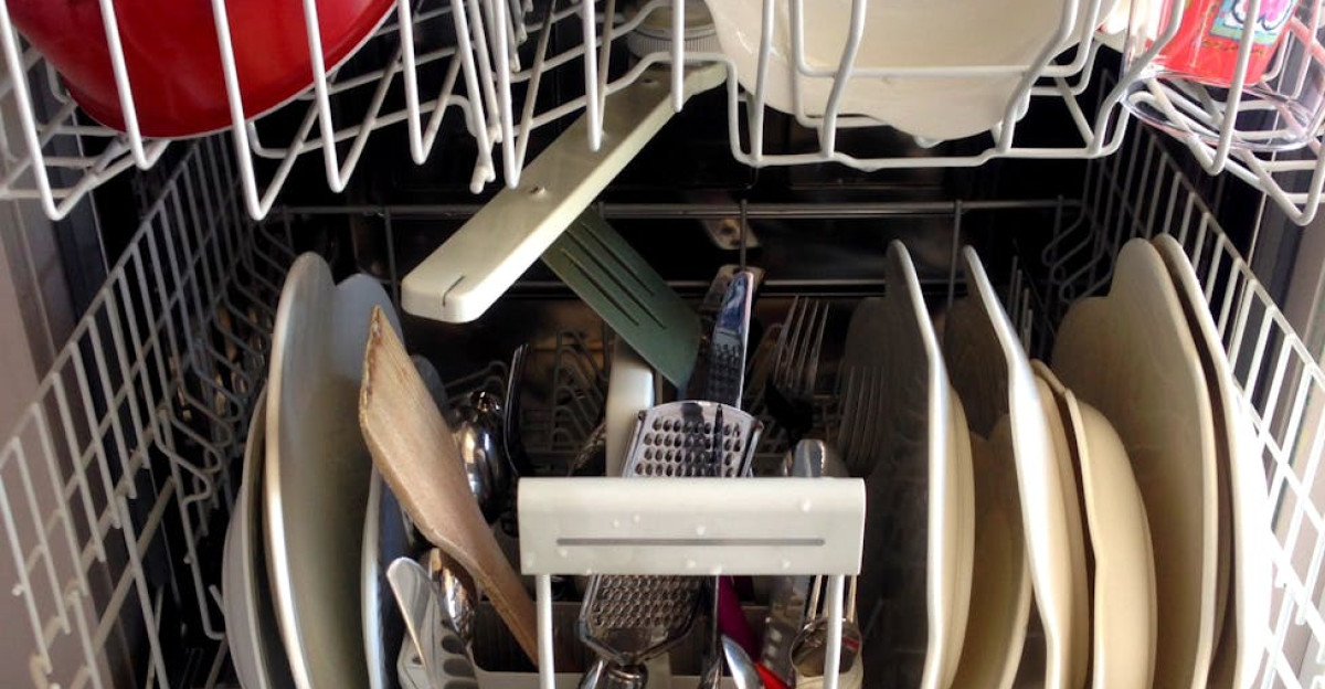 Open dishwasher filled with clean dishes and kitchenware ready for unloading