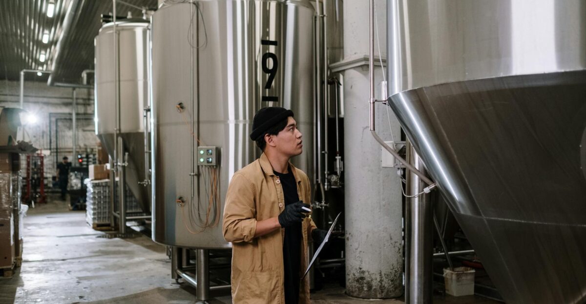 Asian man inspecting stainless steel tanks in a brewery showcasing modern industrial processes