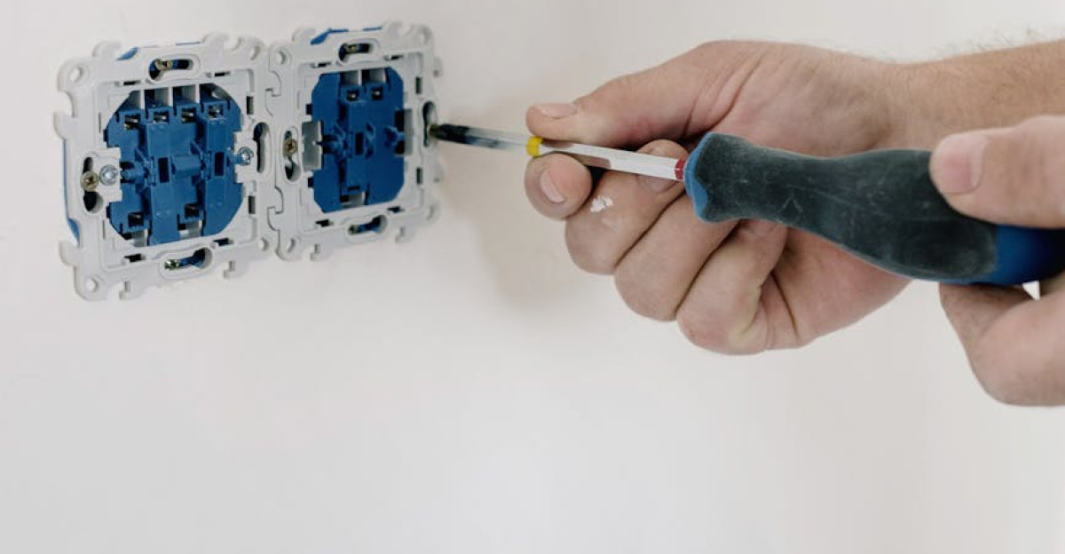 Close-up of hands using a screwdriver to install electrical sockets on a white wall