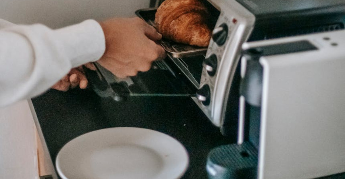 From above of crop anonymous person using microwave oven while heating yummy croissant for breakfast
