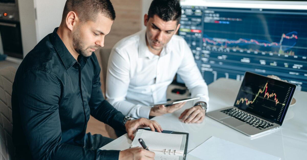 Two businessmen analyzing financial data with digital devices and charts in an office setting