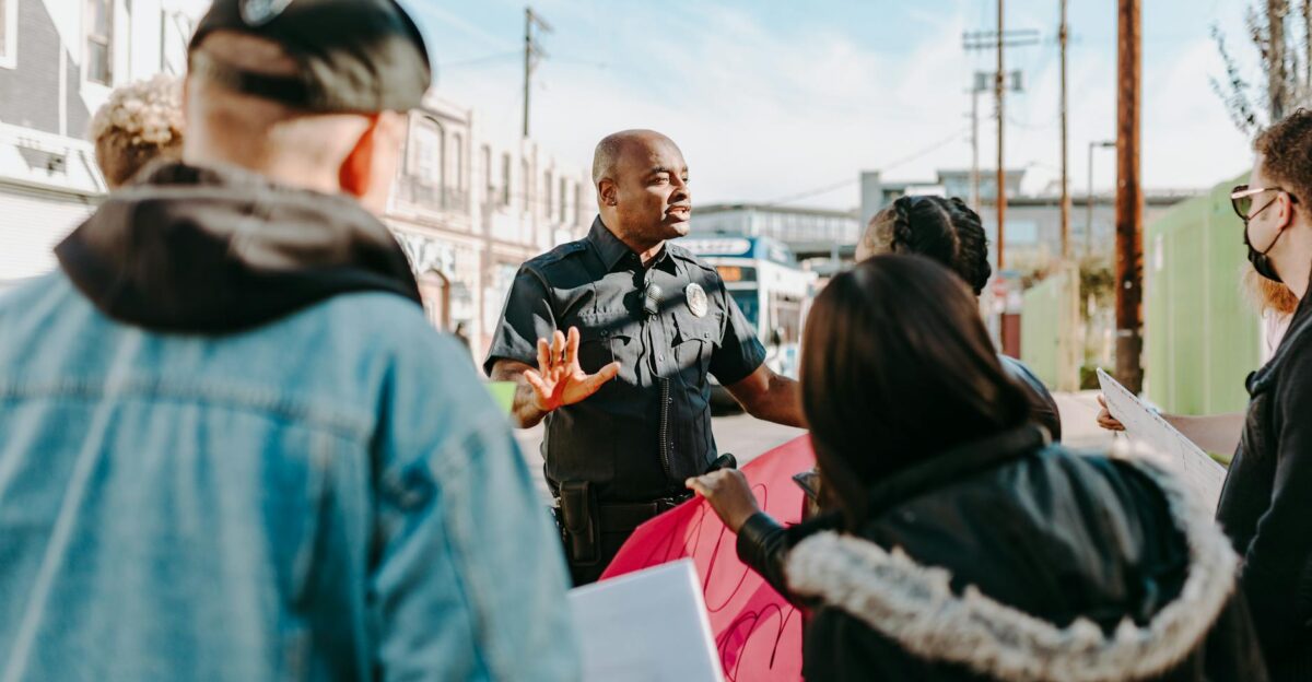 A police officer engaging in conversation with protesters on a sunny street