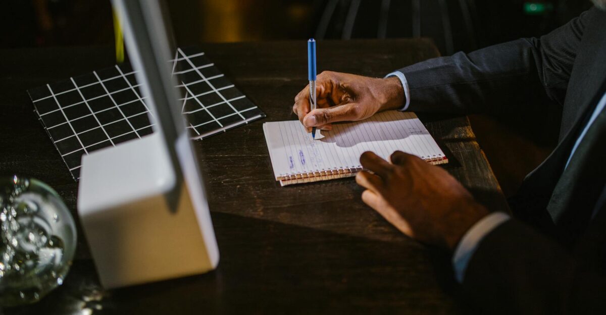 A businessman in a suit writing notes on a notebook at a desk suggesting a professional office environment