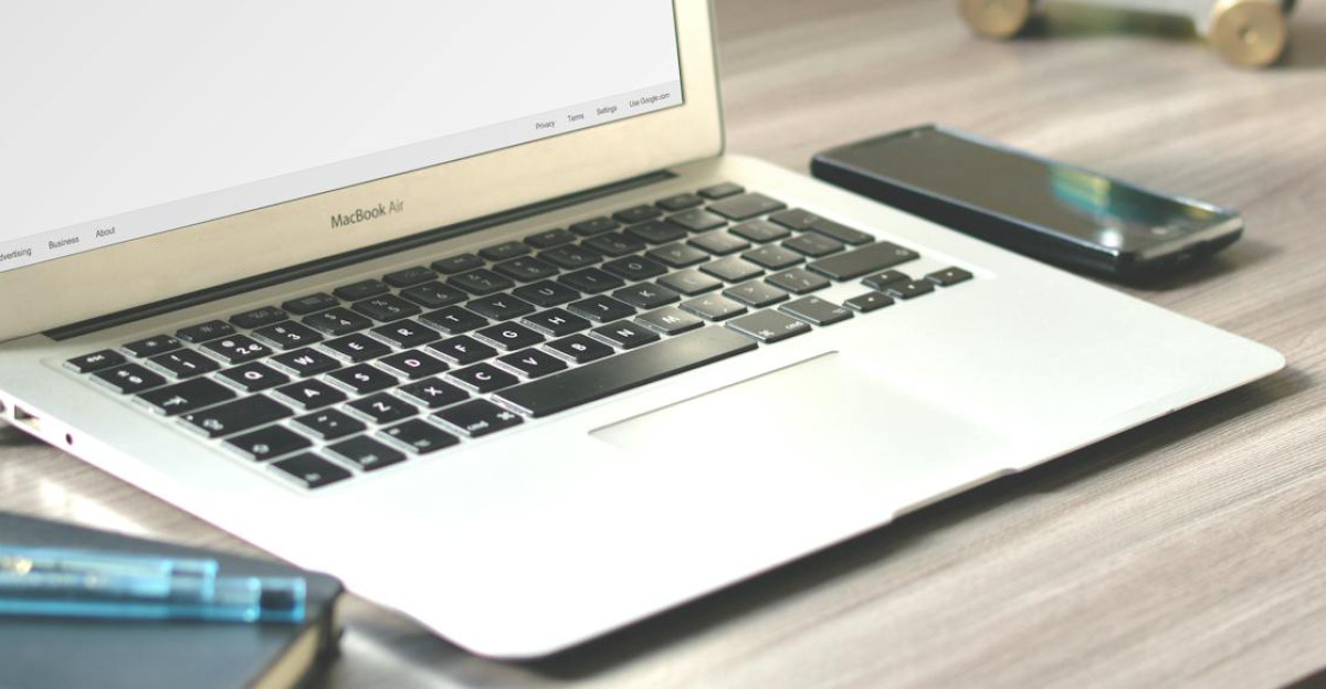 A neat workspace featuring a laptop displaying Google search a smartphone and a notebook on a wooden desk