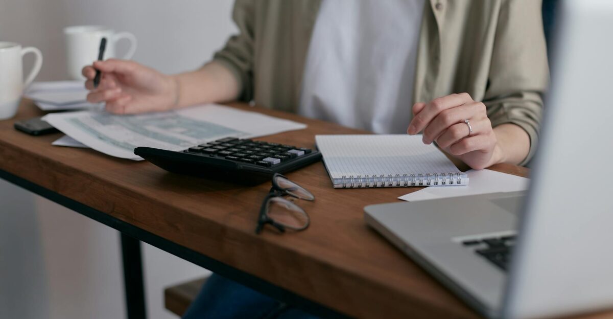 A woman manages finances at home using a laptop and calculator on a wooden desk