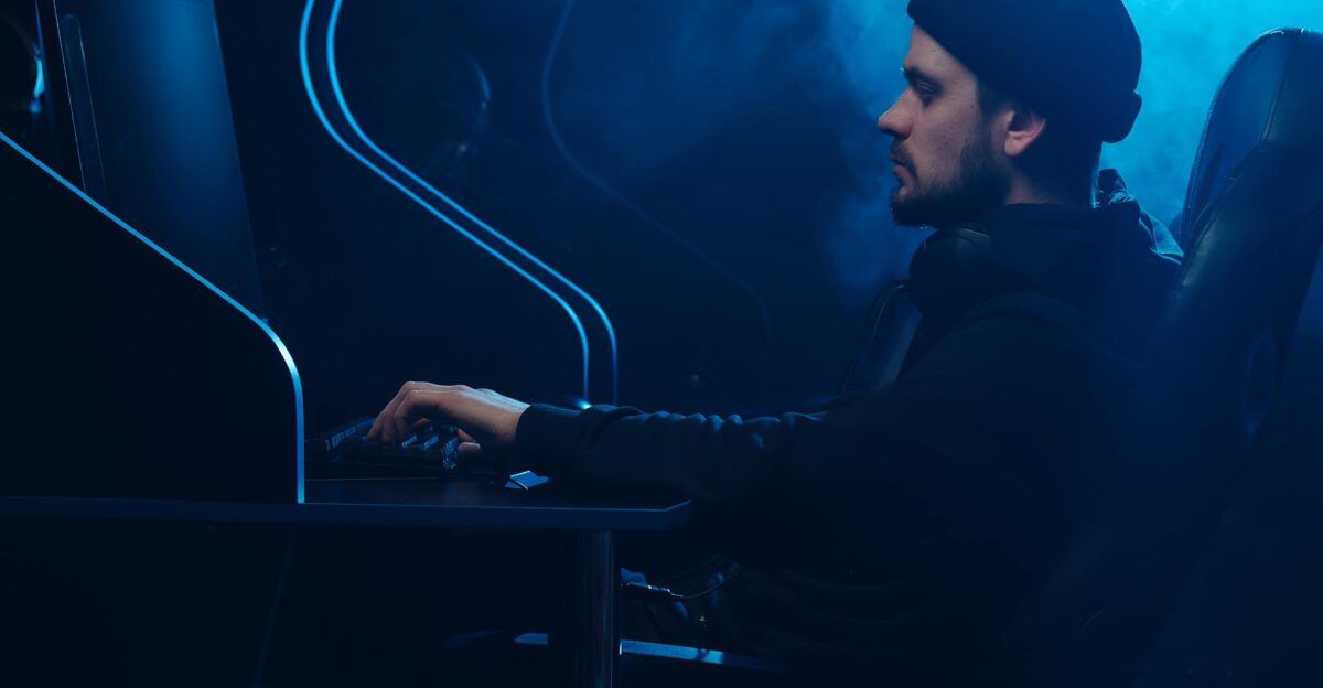 Caucasian man engrossed in gaming on a computer in a dark moody setting