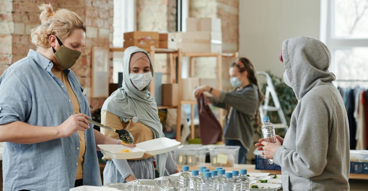 A diverse group of volunteers prepare and distribute food and drinks at an indoor community center