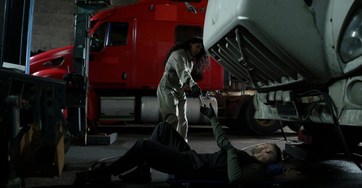 Two mechanics working together to repair a truck in a dimly lit garage setting