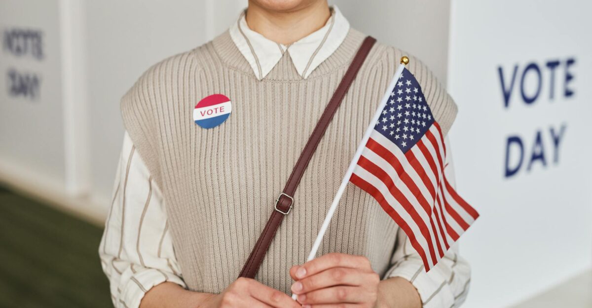 A woman proudly holds the American flag and smiles celebrating voting day