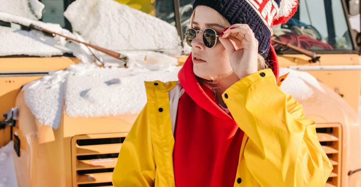 A fashionable woman in winter attire in front of a snow-covered bus enjoying the cold weather