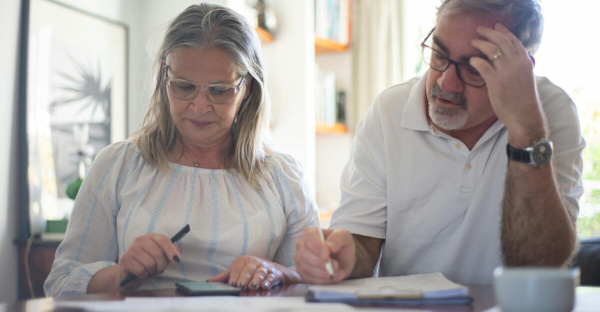 Senior couple calculating expenses at home office desk with documents and notes