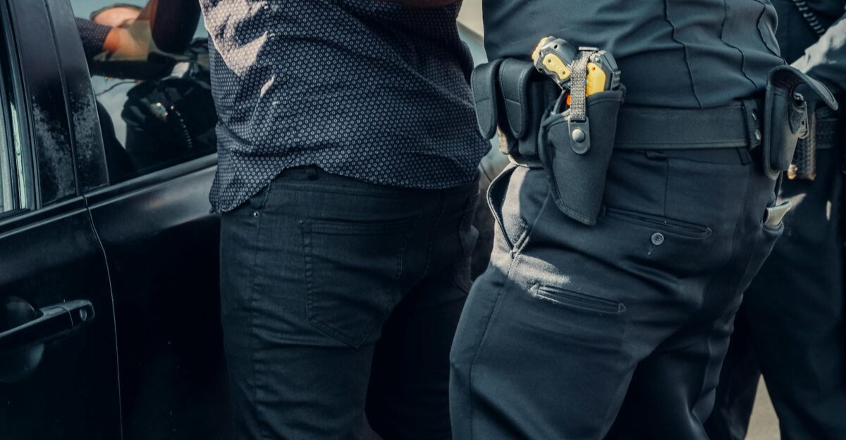 Close-up of police officers detaining a person near a car during daytime