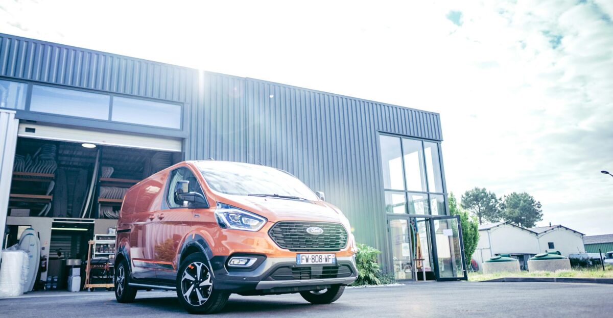 Low angle shot of an orange Ford Tourneo van parked outside a modern industrial building
