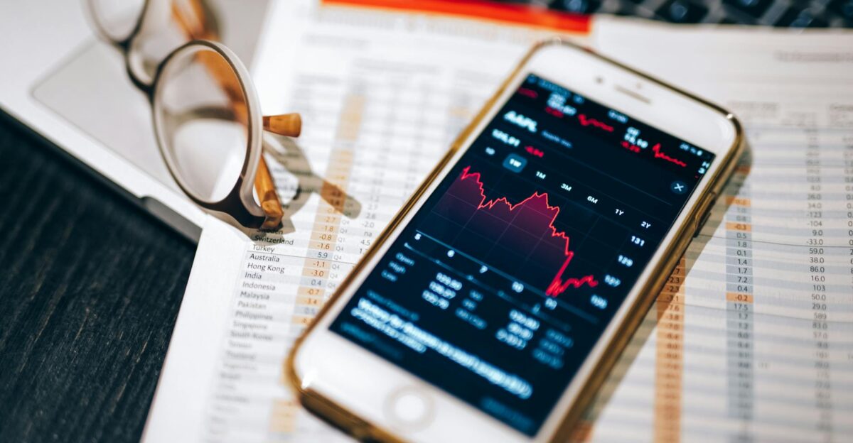 Smartphone displaying stock market chart on a financial spreadsheet with eyeglasses