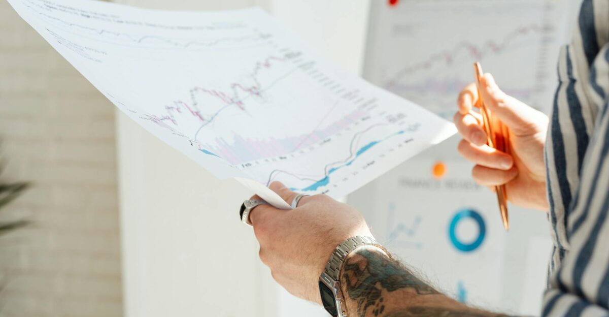 Close-up of a tattooed man s hands holding financial charts with focus on data analysis and stock market trends