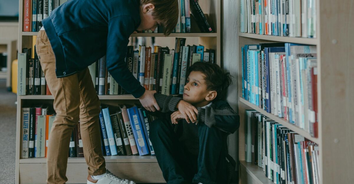 A concerned boy interacting with a classmate sitting on the floor in a library