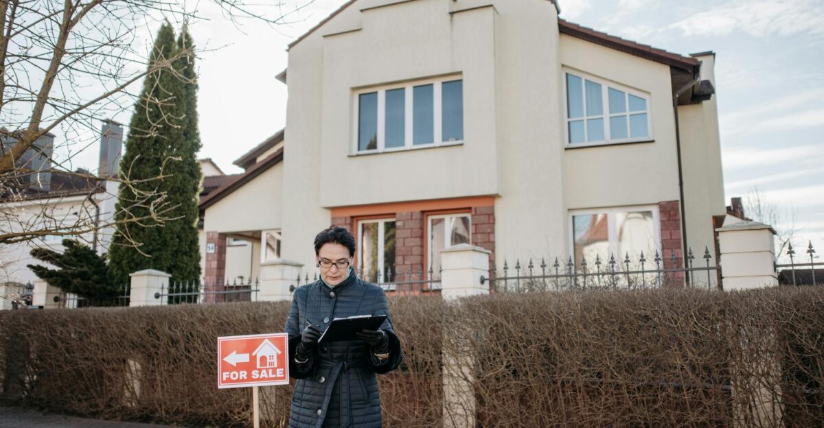 A real estate agent standing outside a house with a For Sale sign ready for viewing