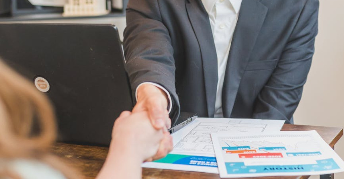 A professional real estate agent welcomes a client in the office with documents on the desk