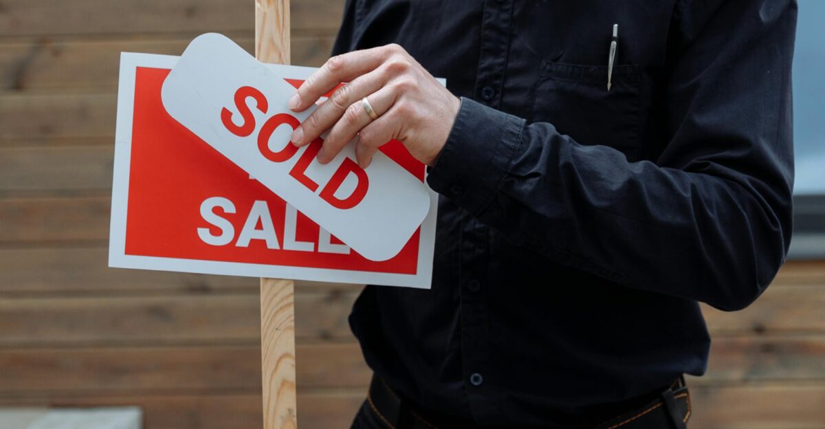 A real estate agent placing a sold sticker over a sale sign indicating successful property deal