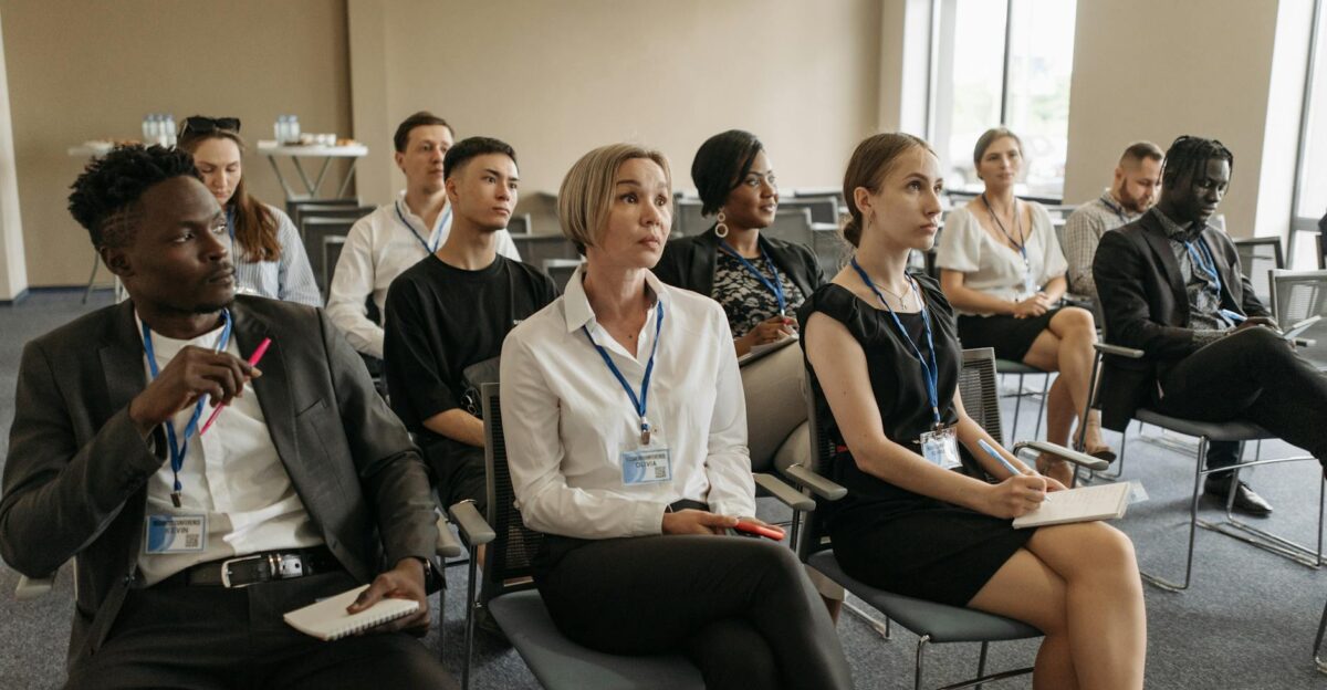 A diverse group of professionals attending an indoor meeting taking notes and listening attentively