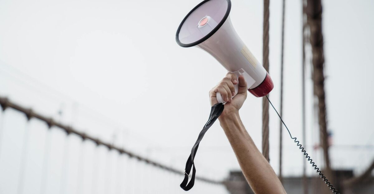 A hand holding a megaphone symbolizing protest or announcement at an outdoor rally