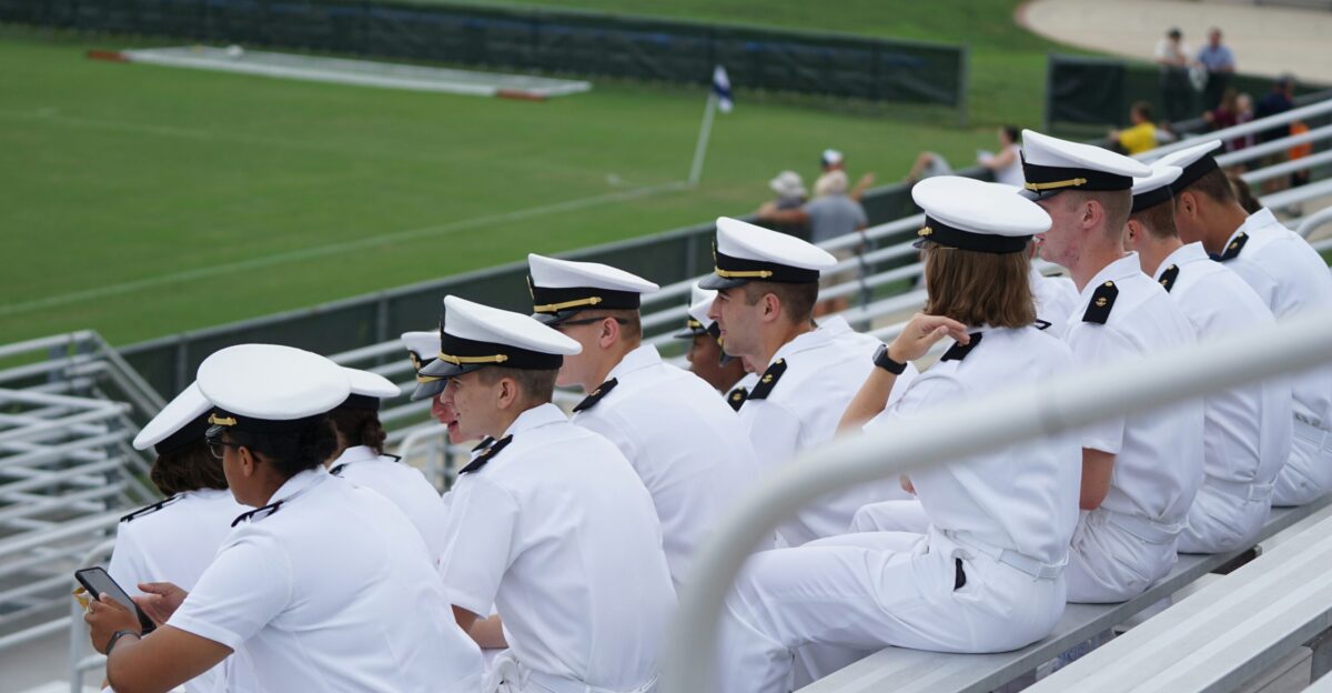 group of people in white uniform sitting looking at field during daytime