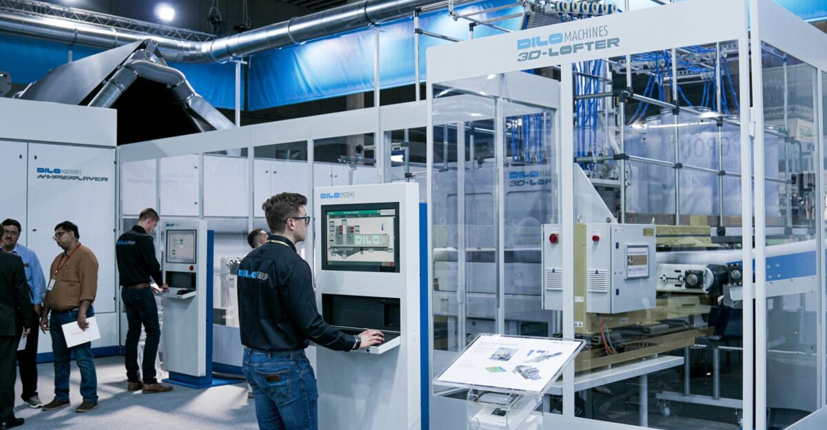 man standing while using computer and another group of men chatting