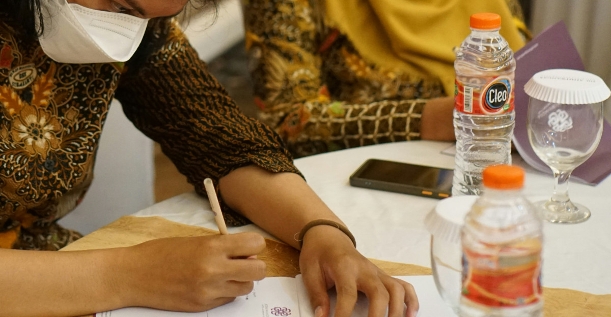 a woman wearing a face mask writing on a piece of paper