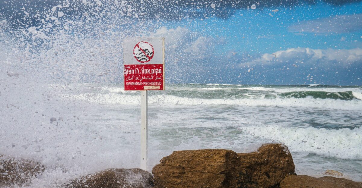 a red and white sign sitting on top of a rock next to the ocean