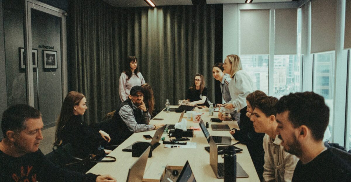 a group of people sitting around a table with laptops