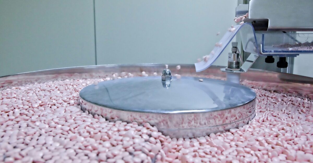 Small pink pills tumbling on a machine surface
