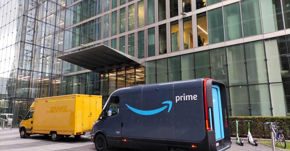 Rivian transporter with Amazon Prime branding parking in front of the Highlight Towers in Munich To the left of it there s a DHL transporter with a combustion engine