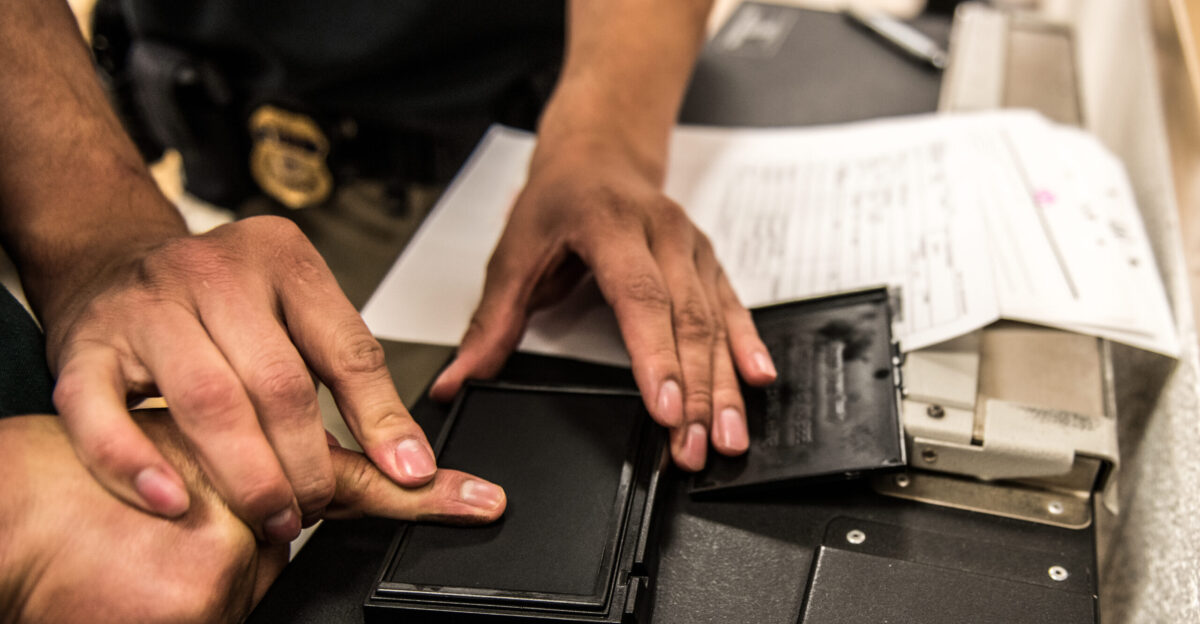 An ICE ERO officer fingerprints someone in custody at a processing center