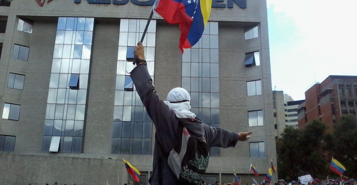 A protester wearing an Anonymous mask and lifting a Venezuelan flag