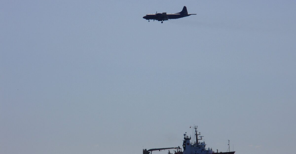 A Canadian Forces Air Command CP-140 Aurora maritime patrol aircraft flies low over a Coast Guard vessel in Lake Ontario during the Canadian International Air Show in Toronto Ontario Canada