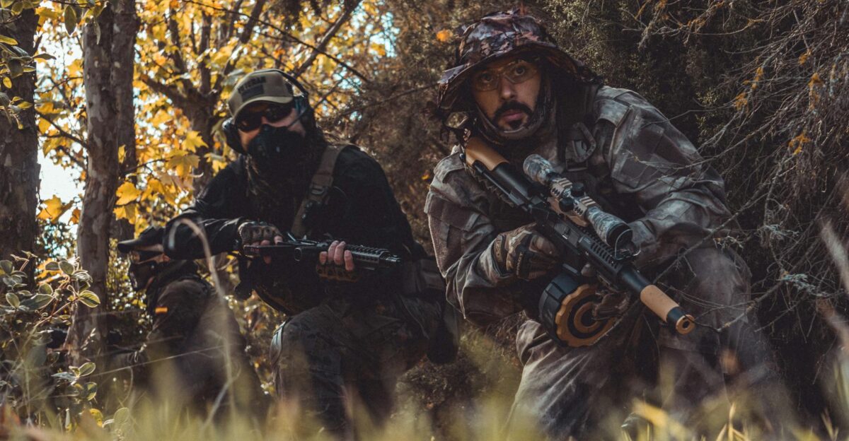 Two soldiers in camouflage gear patrol a forested area ready for combat