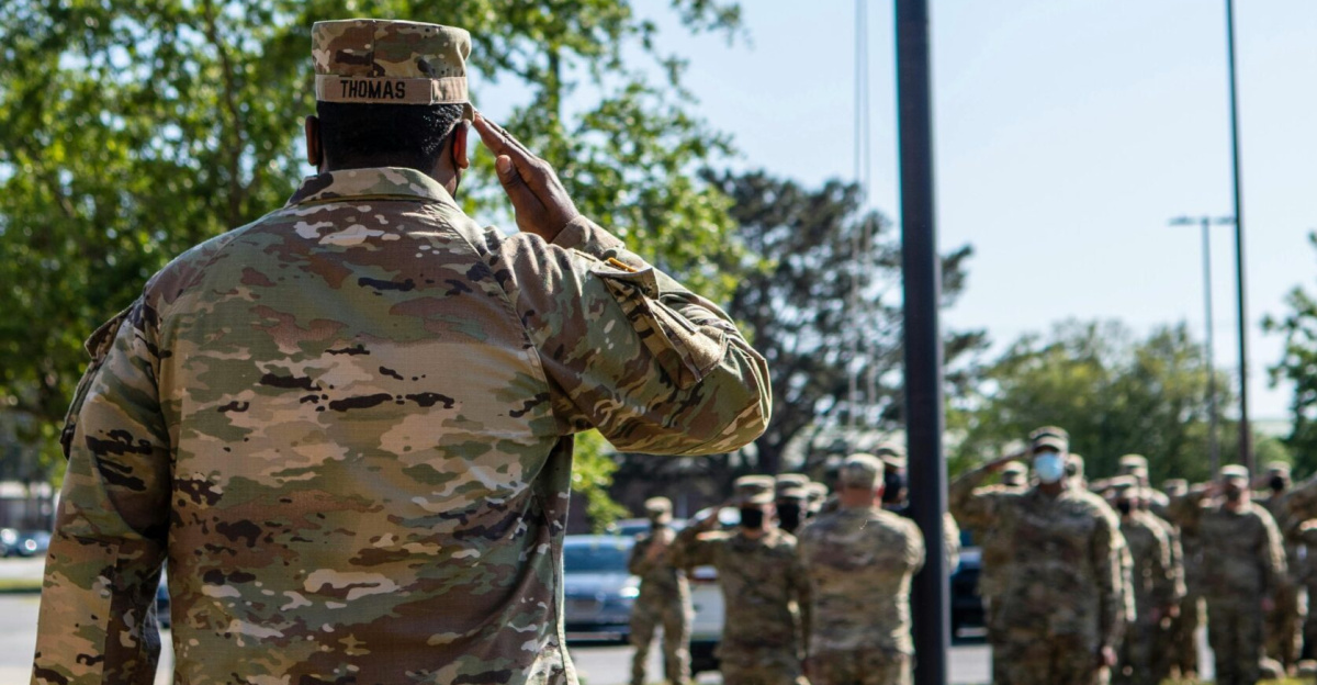 A group of soldiers in uniform salute the American flag during a daytime ceremony.