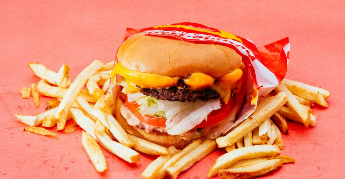 Tasty cheeseburger with fresh ingredients and french fries on a vibrant red background