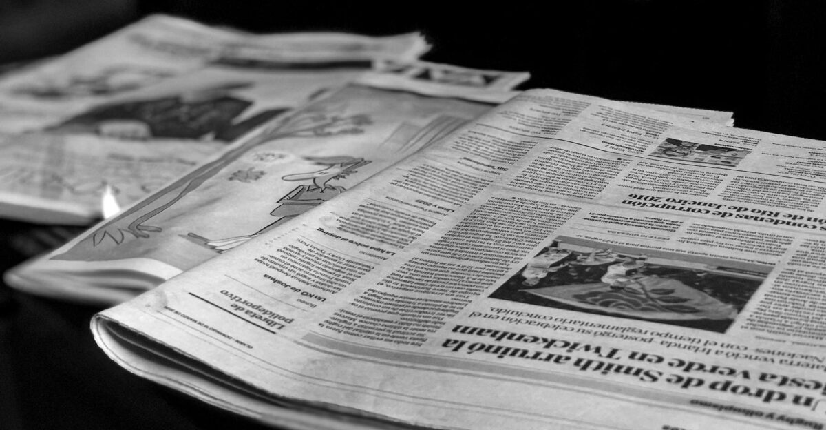 Black and white close-up image of newspapers laid on a table emphasizing print media
