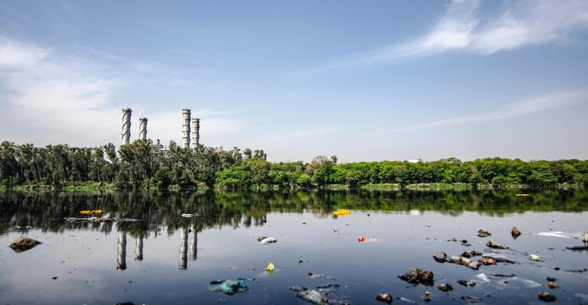 View of a polluted river reflecting factory emissions under a clear sky in India