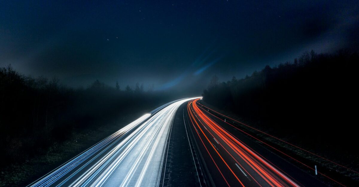 Long exposure night shot capturing stunning red and white light trails on a highway under a starry sky