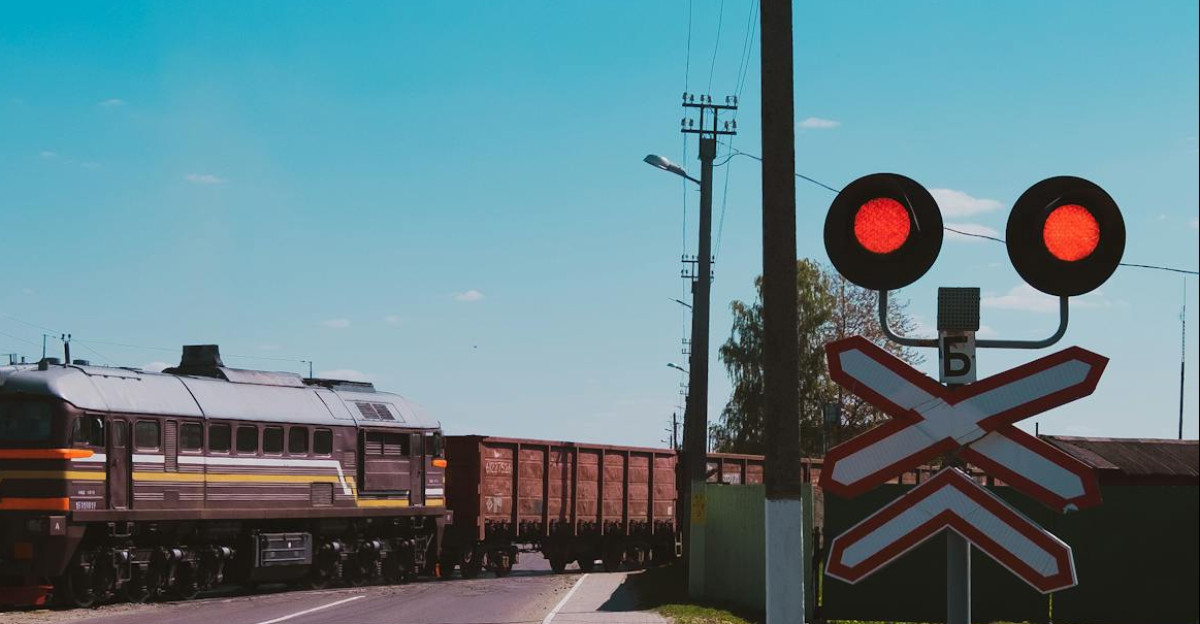 A train crossing a road under a clear blue sky with signal lights indicating stop