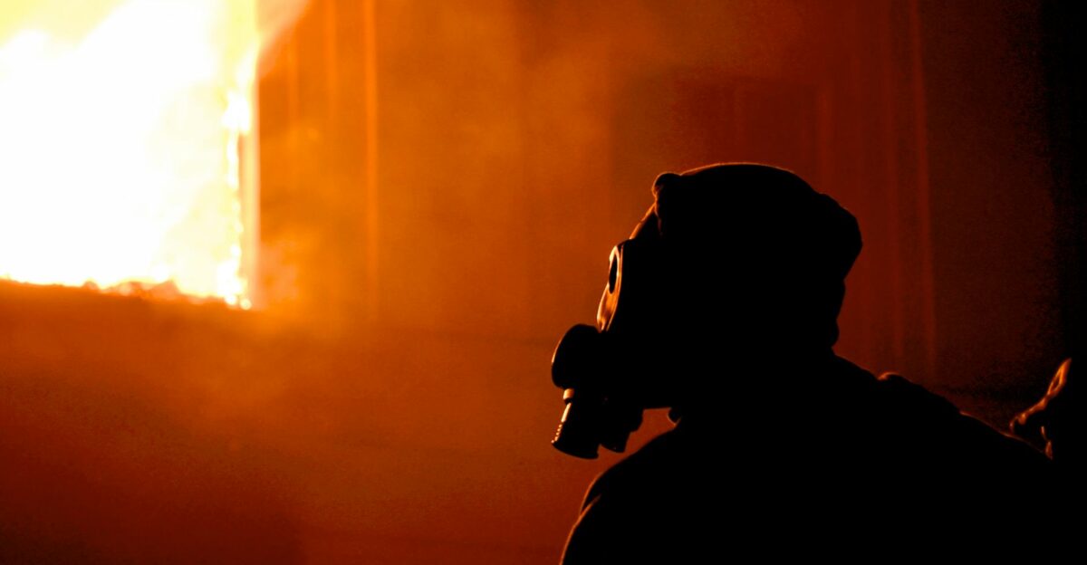 Eerie silhouette of a person with a gas mask in profile facing intense flames and smoke