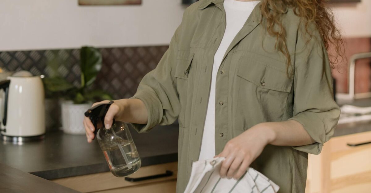 A woman with curly hair cleans a kitchen counter using a spray bottle and cloth