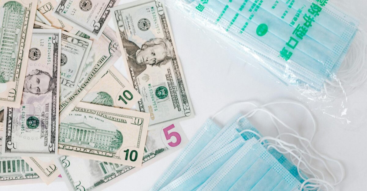 From above composition of stack of USA dollar bills placed near medical protective masks produced in China illustrating concept of medical expenses and deficit during COVID 19