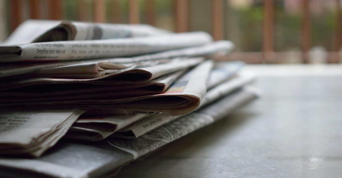A close-up of a stack of newspapers resting on a desk symbolizing information and media