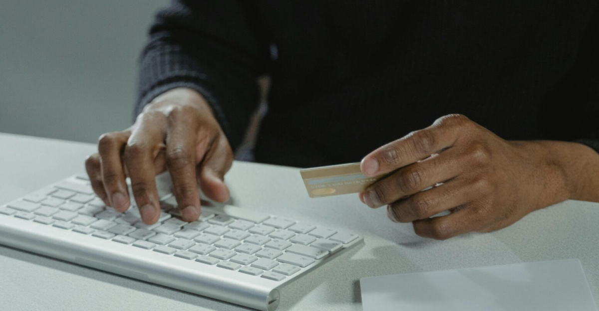 Man with glasses using a keyboard, holding a bank card, surrounded by cash, suggesting online finance or cybercrime themes.